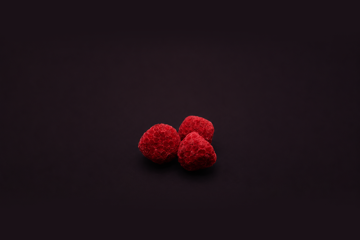 Three vibrant red raspberries clustered together on a dark, solid background.