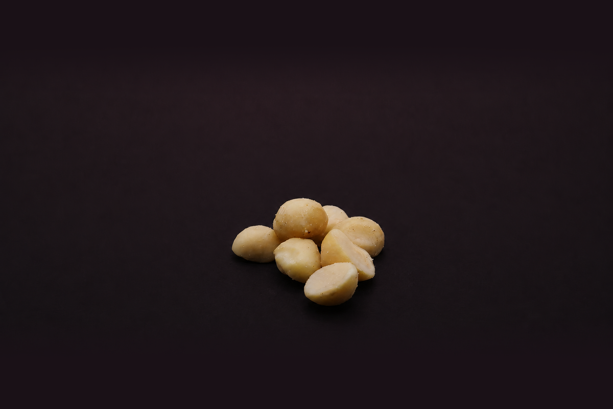 small pile of beige macadamia nut halves on a dark black background.