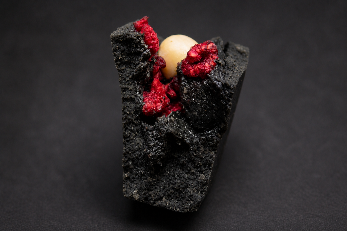 Cut opened black sesame mooncake with raspberry and macadamia filling on a dark background.